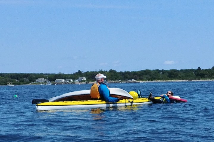 Two people on a kayak in a calm body of water with a shoreline in the background.