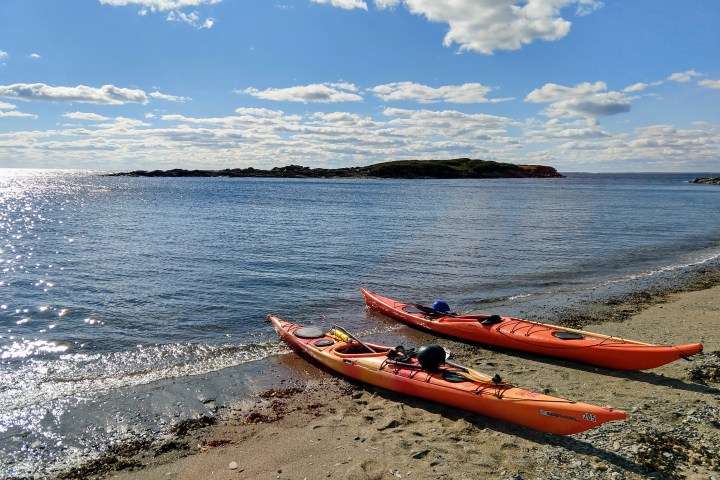 Two orange kayaks on a sandy shore with a calm sea and distant island.