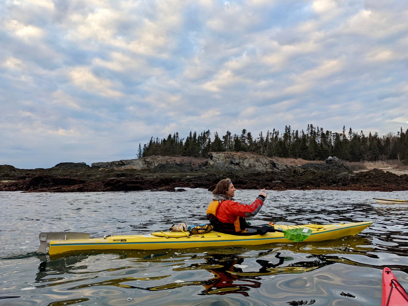 a group of people kayaking along a rocky coastline in Casco Bay.