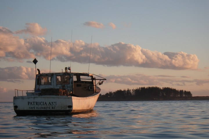 Fishing boat on calm sea at sunset with distant island and clouds.