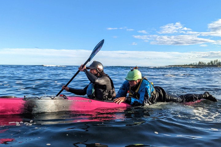 Two people kayaking on the ocean, one paddling and the other lying on the kayak.