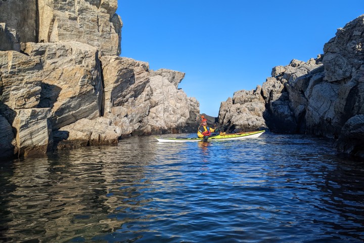 Person kayaking between rocky cliffs under a clear blue sky.