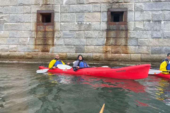 Two people in a red kayak near a stone fort with small windows.