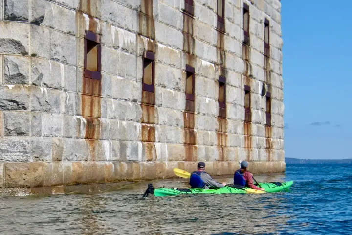 Two people kayaking next to a large stone Fort in the ocean