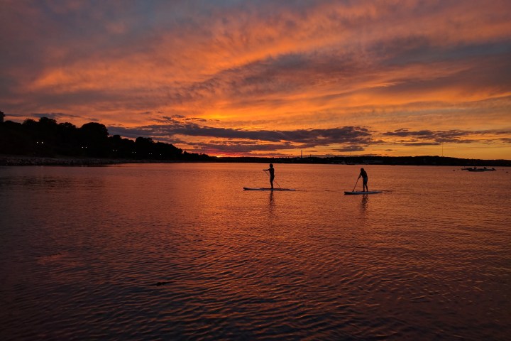 Two paddle boarders on a lake at sunset with a vibrant orange sky.