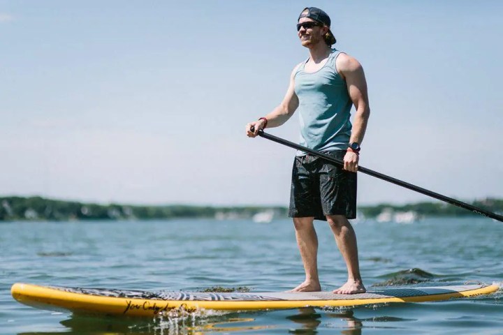 Man paddleboarding on the ocean. Wearing a tank top and shorts.