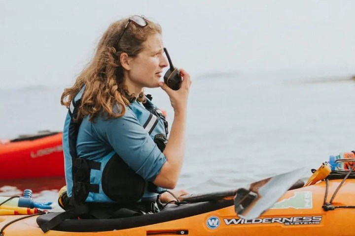 Person in a kayak on water using a walkie-talkie.