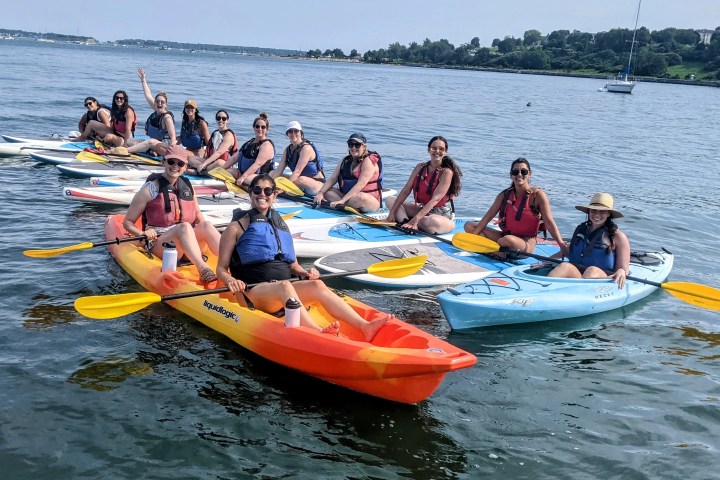 Group of people on kayaks and paddleboards on a calm lake, wearing life vests and smiling.