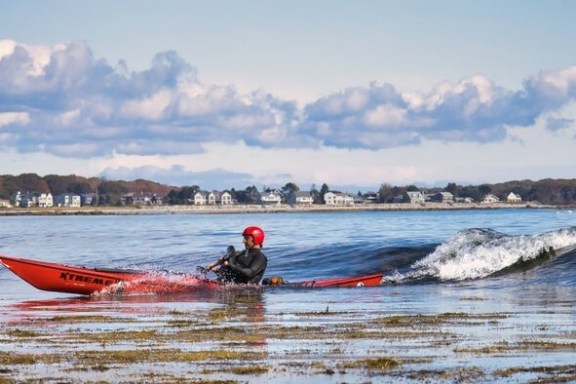 Joe G surfing a sea kayak at a Maine beach