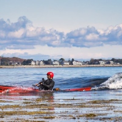 Joe G surfing a sea kayak at a Maine beach