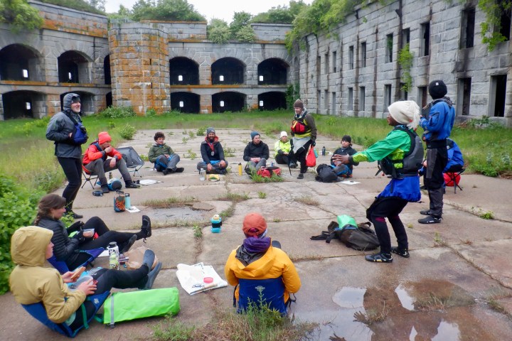 Group of people in outdoor gear sit in a circle in an old stone fort.
