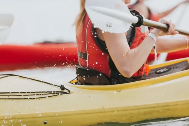 Person kayaking in a yellow kayak with a red life vest, paddling in water.