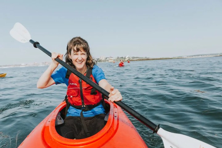 Woman in a red kayak paddling on a sunny day with a smile.