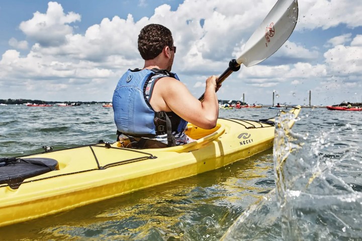 Person kayaking on a lake with a bright yellow kayak under a blue, cloudy sky.
