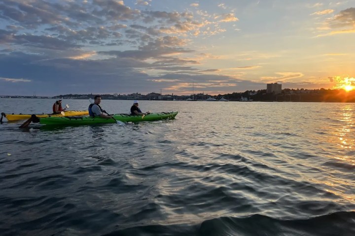 People kayaking on calm water at sunset with cloudy sky.