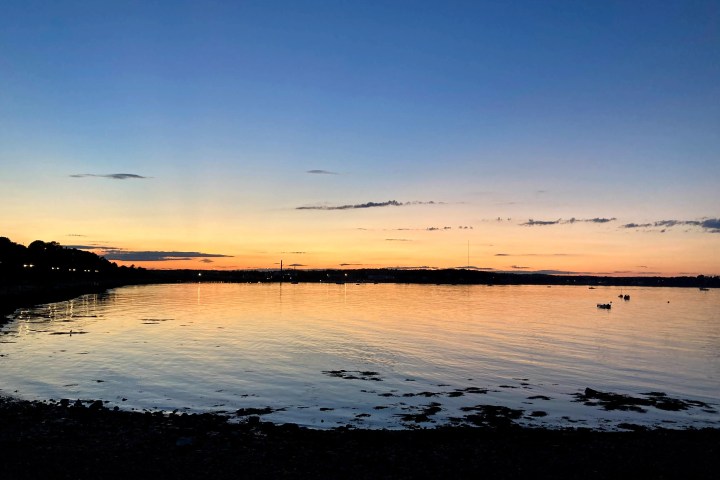 Tranquil sunset over a calm bay with silhouettes of land on both sides.