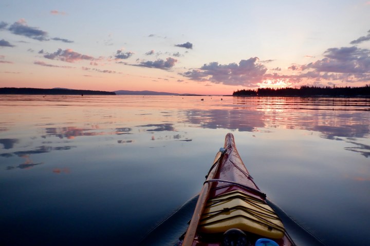 Kayak on calm water at sunset with pink and orange sky.