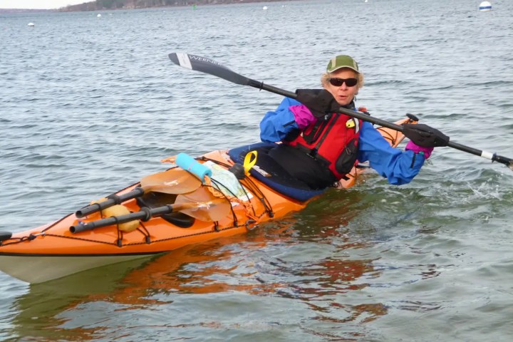 Person kayaking in orange kayak on water, wearing blue jacket and cap.