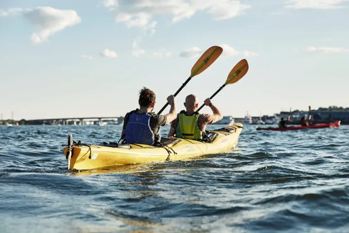 Two people kayaking in a yellow kayak on a sunny day.