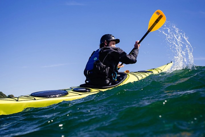 Person kayaking on blue ocean with a yellow kayak and a bright blue sky.