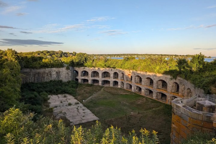 Ruins of a historic fort with stone arches surrounded by greenery and a distant water view.