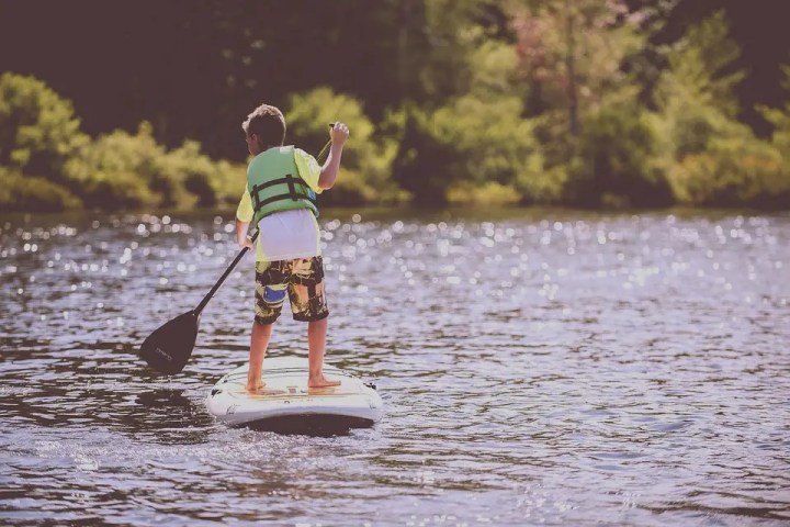 Child paddleboarding on a lake with trees in the background.