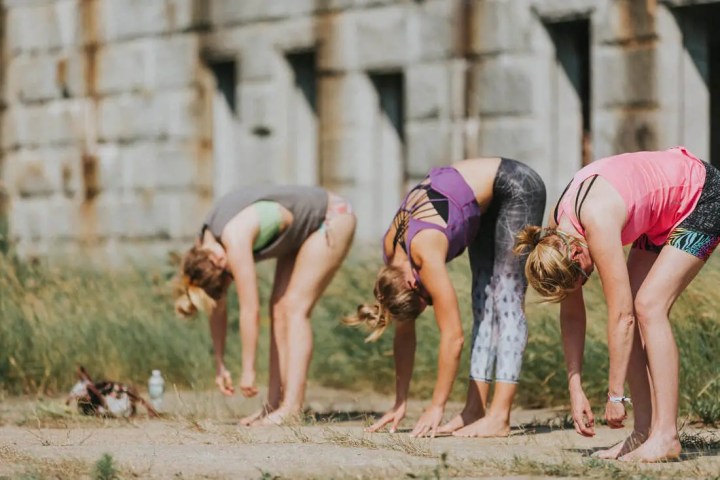 Three women doing yoga poses outdoors near an old building.