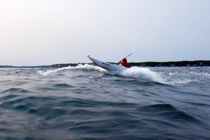 Person kayaking on rough sea waves with a distant shoreline visible.