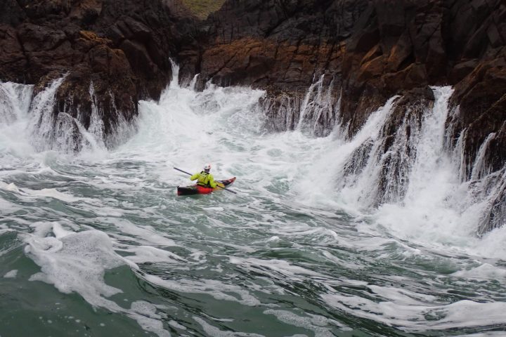 Joe H beneath large pour overs rock gardening in a sea kayak