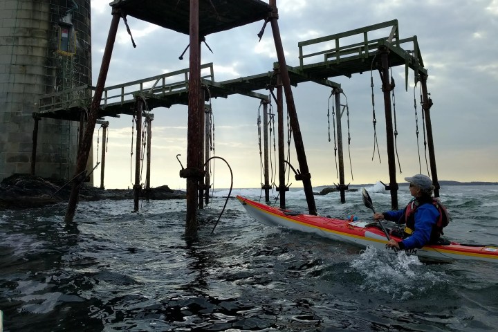 A kayaker paddling near a lighthouse and a metal structure on a cloudy day.