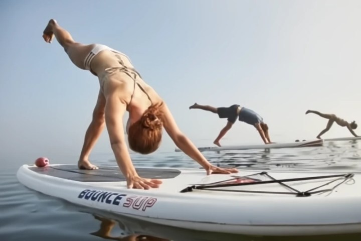 Three people practicing yoga poses on paddleboards on calm water.