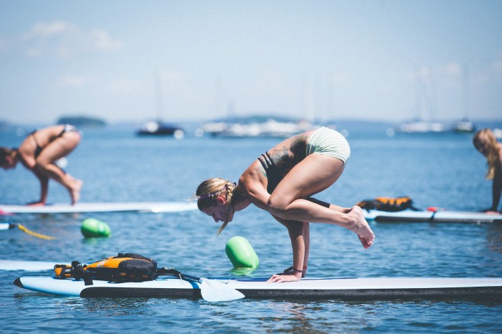 People doing yoga poses on paddleboards in a calm body of water with distant boats.