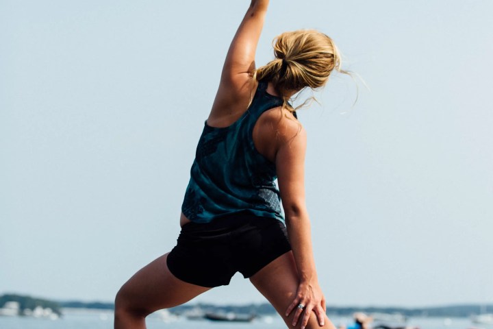Person doing yoga pose on a stand-up paddleboard in calm water, with a clear sky background.