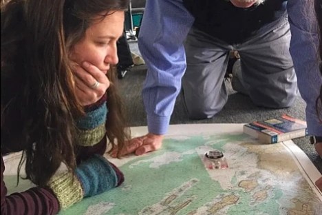 Two people examining a large map on the floor, one using a compass.