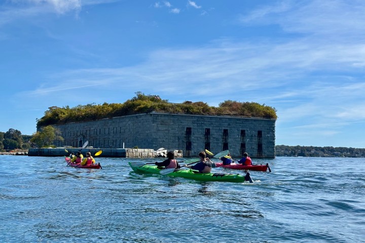 People kayaking near a stone fort on a sunny day.