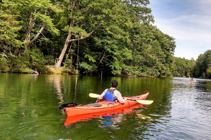 a man riding on the back of a boat next to a lake
