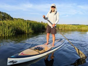 a person standing on a paddleboard in a grassy waterway