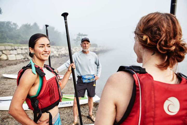 Two people stand by the water right before paddleboarding