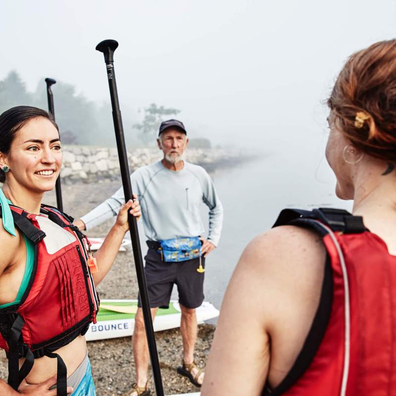 Two people stand by the water right before paddleboarding