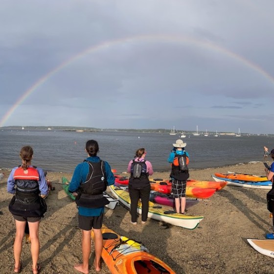 Paddlers take a break before the start of a race to watch a rainbow on the beach