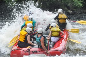People getting hit by a wave in a raft