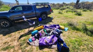 Rafting equipment being packed in a field, a pickup truck and cactuses in the background