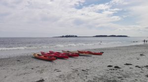 Sea kayaks on a sandy beach getting ready to launch, with and island and headland in the background