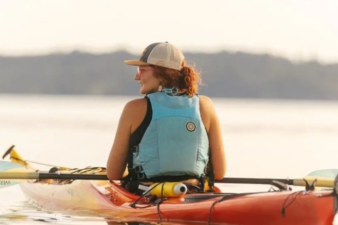 a woman sitting in a sea kayak at sunset