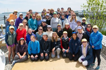 A group of 20-30 women pose for a photo with the ocean in the background