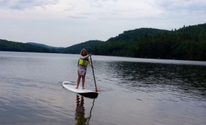 A girl on a paddleboard in a lake with hills and mountains in the background