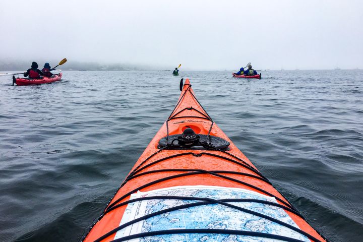 View from a kayak showing foggy sea with other kayakers in the distance.