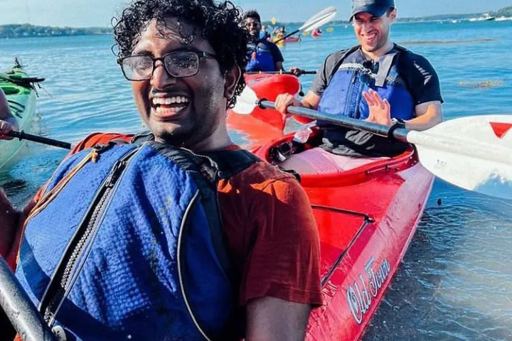 People kayaking on a sunny day, smiling and wearing life vests in a red kayak.