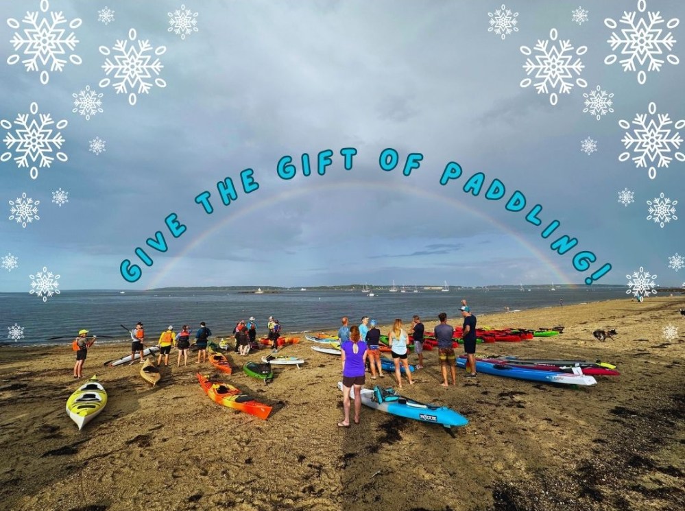Group of people with kayaks on beach under rainbow with text 'Give the Gift of Paddling!' and snowflake decor.