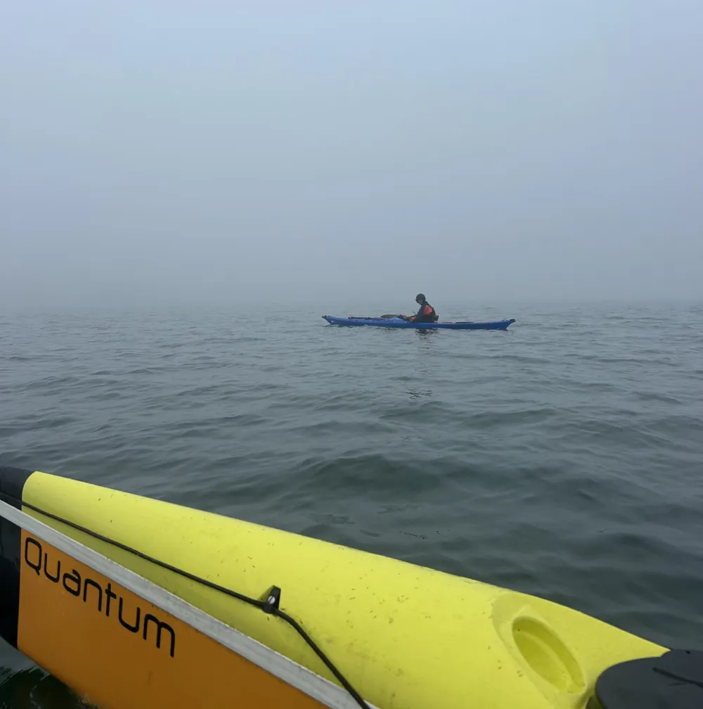 Person kayaking in foggy water, with a yellow kayak nearby labeled 'Quantum'.